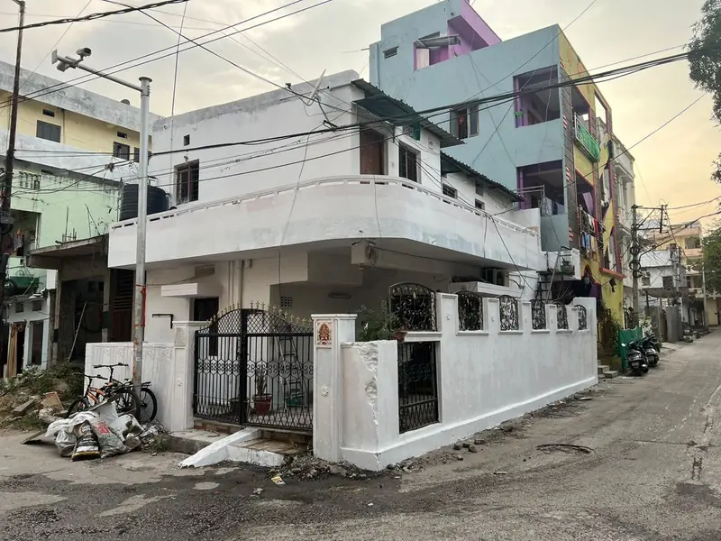 Corner house in Hyderabad before exterior repainting, with weathered white walls and stained compound wall