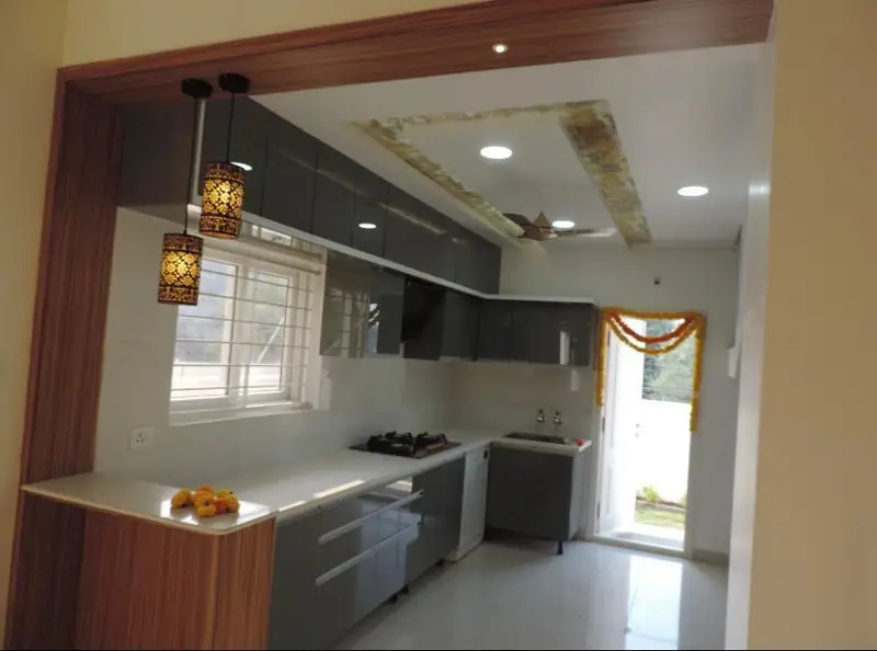 Grey high-gloss modular kitchen with white counter and a stone-effect false ceiling, completed by The Wall Fashion